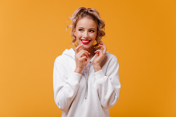 Wall Mural - Cheerful girl with beautiful smile, insidiously looks away. Studio photo on bright background of cute European model