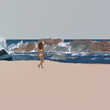 Młoda kobieta w stroju kąpielowym spacerująca po plaży  w słonecznej Kalifornii