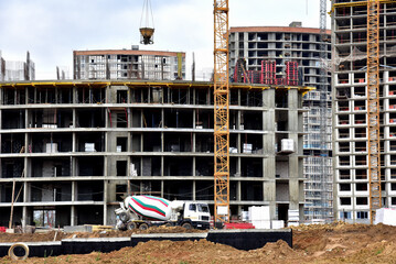 Poster - Cement  mixer truck working pouring mix into crane concrete bucket. View of larger construction site where tower cranes are building residential buildings, multi-storey offices and modern skyscrapers