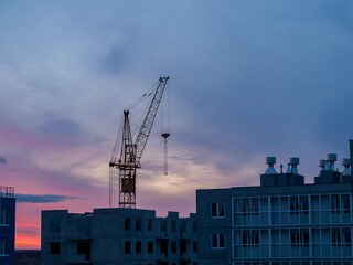 high-rise crane in the construction of high-rise buildings in the city district, against the background of the sunset