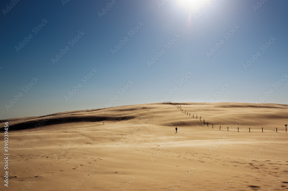 Krajobraz pustynny błękitne niebo i ruchome piaski  z sylwetką idącego człowieka w pięknym świetle zachodzącego słońca - obrazy, fototapety, plakaty 