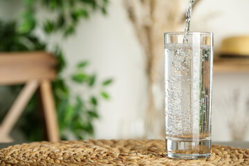 Pouring water into glass on table indoors, space for text. Refreshing drink