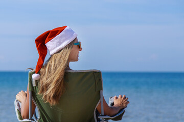 travel on New year's eve on beach by sea. girl in Christmas hat is sunbathing in sun. woma,n with dark glasses. woman in chair with her back to camera looks into distance. Tourist resting by water.