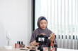 © Orathai - Muslim women making video beauty vlogger bloggers doing a cosmetic makeup tutorial vlog with brushes looking camera Save clips and share them on social media live via the internet Online