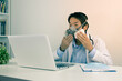 © steafpong - Young Asian Doctor Man in Lab Coat or Gown with Stethoscope Demonstrate Filter Mask Using with Patient Via Laptop Computer in Office in Vintage Tone