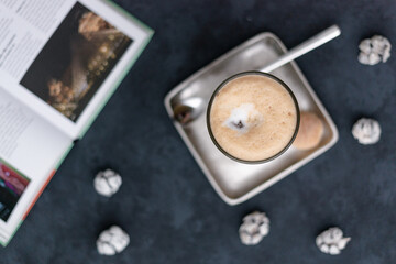 Sticker - Top view of a coffee latte on a square saucer with a spoon, cookies, and crinkles on a black table