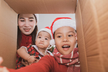 Wall Mural - merry christmas and happy holidays. parent and two little children opening a christmas present. little kid having fun near christmas tree indoors. view from inside of the box. child playing at home