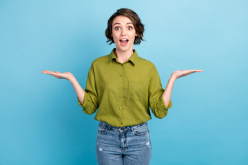 Photo of lovely charming lady short hairstyle excited look camera hold two hands empty space open mouth wear denim jeans green shirt isolated blue color background