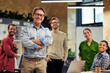 © Friends Stock - Happy startup team. Group of cheerful multiracial business people smiling at camera while standing in the modern office, working together