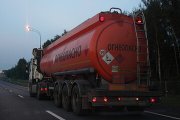 Orange barrel semi fuel truck with 30 1202 DIESEL dangerous class sign and Russian inscription FLAMMABLE drive on suburban highway at summer evening in perspective, rear side view ADR hazardous cargo