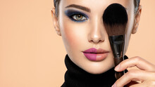 Portrait Of A Girl With Cosmetic Brush At Face. Woman Covering One Eye On The Face Using Makeup Brush. One Half Face Of A Beautiful White Woman With  Bright Makeup And The Other Is Natural.