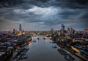 Elevated, moody view to the illuminated skyline of London, United Kingdom, with a cloudy sky during dusk