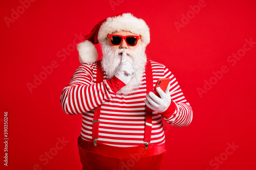 Portrait of his he nice handsome mysterious bearded fat Santa using device app 5g shopping secret sale discount showing shh sign silence mute isolated bright vivid shine vibrant red color background