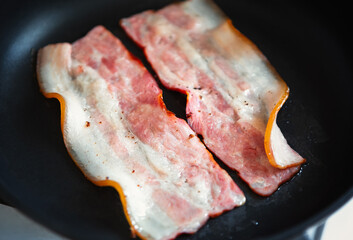 Cooking English breakfast meal at home kitchen.Two strips of pork bacon frying on hot pan in close up photo