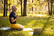Calm mature male doing meditation with laptop outdoors