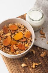 Canvas Print - top view of delicious granola with nuts, dried apricots and yogurt on wooden board on white background