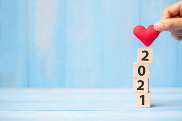 Business man hand holding red heart shape over 2021 wooden cubes on blue table background with copy space for text. Business, Resolution, New Year New You and Happy Valentine’s day holiday concept