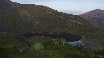 Canvas Print - A wild camping man and tent overlooking a beautiful mountain lake in Snowdonia National Park