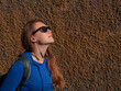 © KawaiiS - Young woman in blue hoody and black sunglasses on plaster wall background listening to music and podcasts with Wi-Fi headphones. Hipster lady in wireless earphones brown urban backdrop. Lifestyle blog