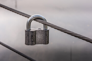 Metal padlock on steel cable of city bridge fence