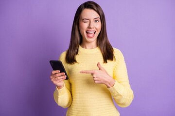 Sticker - Photo portrait of woman holding phone in one hand pointing finger winking with eye open mouth isolated on vivid purple colored background