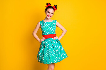 Poster - Portrait of nice charming cheery girl wearing teal dotted dress hands on hips isolated over vibrant yellow color background