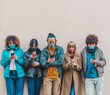 © Davide Angelini - Multiracial friends using mobile phone tracking Coronavirus spread - New normal lifestyle concept with young people covered by face mask watching smartphone.