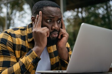 Portrait of pensive African American man using laptop computer, looking at digital screen, watching movie, reading news. Serious student studying online, learning something