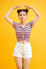 Beauty fashion model girl with two pink bun hairstyle and colourful make-up isolated on yellow background