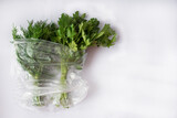 Fototapeta Tulipany - green fresh drill and parsley in transparent plastic bag lie on white background. Copy space for text. Healthy vitamin herbs