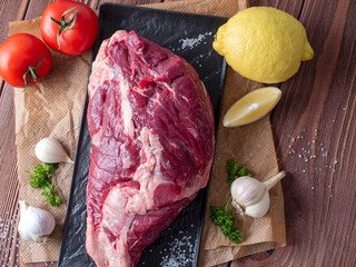 Canvas Print - a piece of raw black Angus beef sits on a black plate. Around fresh tomatoes, herbs, lemon, garlic. Wooden background, top view, flat lay.