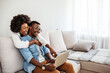 © Dragana Gordic - Happy mixed race young couple using laptop looking at screen together watching video movie sit on sofa, smiling interracial husband and wife make online computer call do internet shopping at home