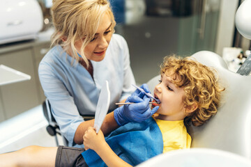 Wall Mural - Cute young boy visiting dentist, having his teeth checked by female dentist in dental office.