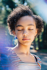 Potrait of teen girl with eyes closed standing outside in sunlight