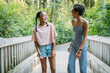 © Inti St. Clair - Teen girls walking and laughing together on bridge in nature park