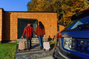 Lovely caucasian family moving to new house goes with suitcases to enter new home.