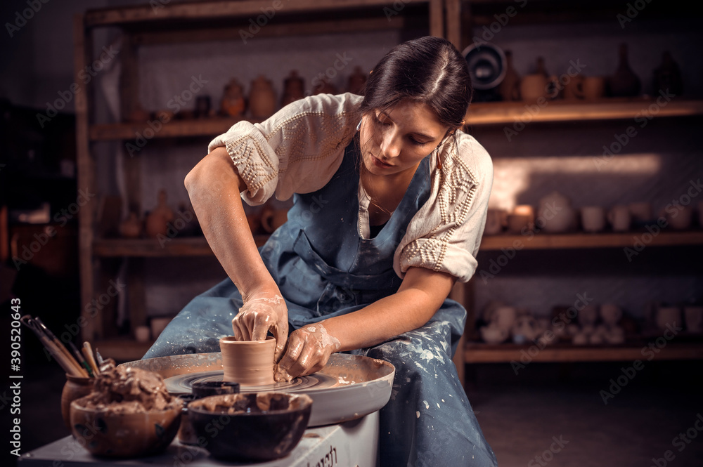 Charming craftsman works with clay on a potter's wheel. The concept of craft creativity. - obrazy, fototapety, plakaty 