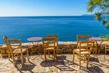 Fototapeta Do akwarium - Traditional cafe exterior in the fortified medieval  castle of Monemvasia. Iron tables and wooden chairs with the view of the  aegean sea in the background.