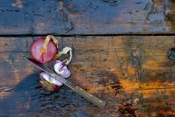 Purple Crimean onion on a wooden surface. Two bulbs in husk, one cut in half with a knife.