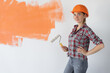 © Andrii Lysenko - woman dressed in an orange safety helmet holds a roller in her hand. home renovation concept