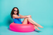 Photo of pretty cute lovely young lady model sit inflatable pink ring posing photographer toothy smile summer seaside ocean resort advert wear blue swimsuit isolated teal color background