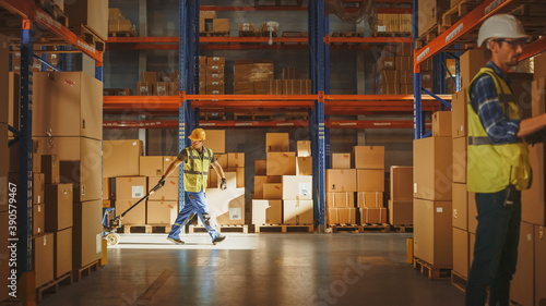 Worker Moves Cardboard Boxes using Hand Pallet Truck, Walking between Rows of Shelves with Goods in Retail Warehouse. People Work in Product Distribution Logistics Center. Side View Shot