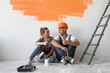 © Andrii Lysenko - home renovation concept, man and woman sit on the floor near the wall with orange stain. Raise your thumb up.