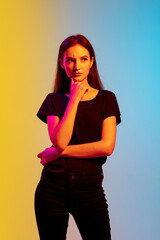 Wall Mural - Thoughtful, dreamful. Young caucasian woman's portrait on gradient blue-yellow studio background in neon light. Concept of youth, human emotions, facial expression, sales, ad. Beautiful brunette model