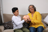 Fototapeta Panele - Indian/asian Grandma teaching her grand son importance of savings, putting coins into pink piggy bank.