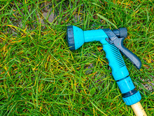 Blue Gun Spray Water On The Hose For Watering The Lawn. Blue Spray Gun For Watering Green Grass. Irrigation Of The Garden With A Garden Hose. Gardening. Farming. Agriculture. Place For Your Text.