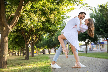 Lovely young couple dancing together in park on sunny day