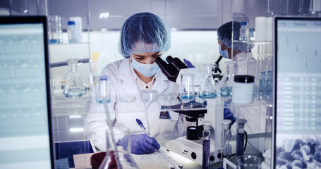 Wall Mural - female science team working on biohazardous samples. using microscope and computer with data
