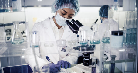 Wall Mural - female science team working on biohazardous samples. using microscope and computer with data