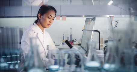 Wall Mural - asian female doctor working in futuristic laboratory. using microscope and computer for blood sample
